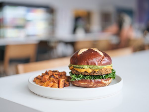 Love Life Burger with a vegan patty, kale, sauces, on a pretzel bun on a plate next to a side of fries