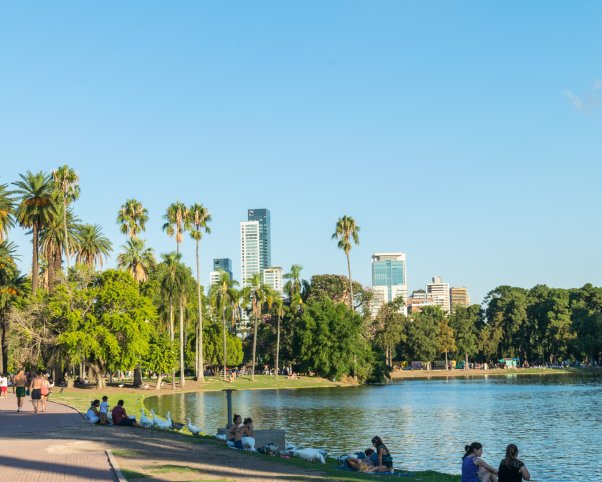 lagos de palermo park in buenos aires, argentina with people sitting along the lakeside and tall buildings in the distance