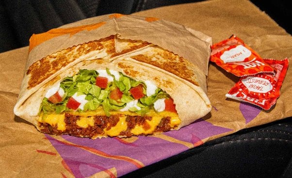 taco bell's vegan crunchwrap on a taco bell bag next to packets of hot sauce