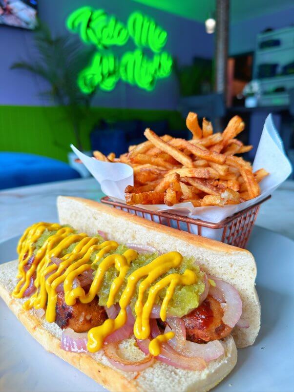 vegan dog topped with onions and mustard in front of a basket of french fries