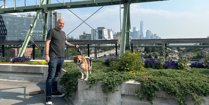 man holding a leash next to a beagle in front of a city background