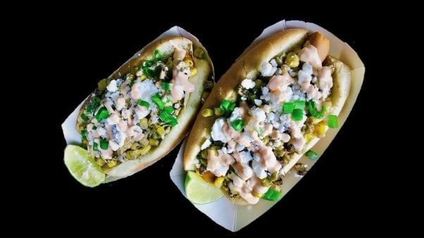 two vegan hot dogs topped with esquites, vegan feta, cilantro, and a sauce