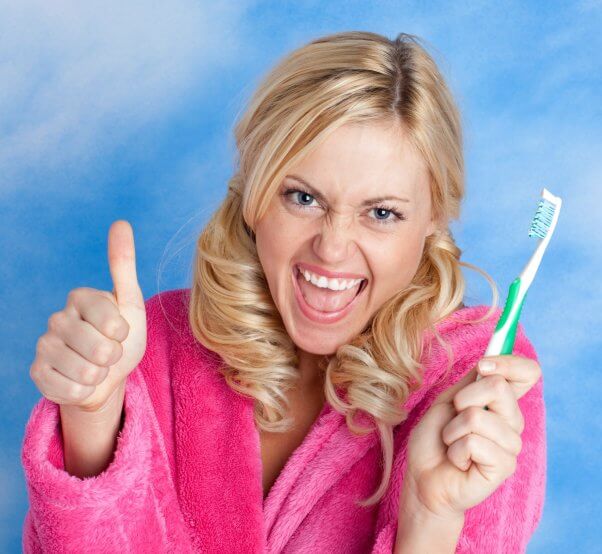 A woman wearing a pink bath rob holds up a toothbrush and a thumbs up