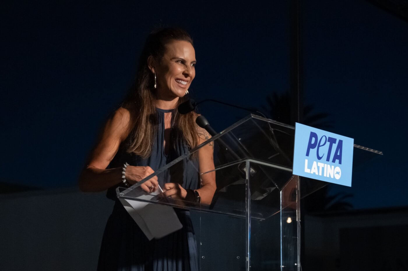 Kate del Castillo smiling and speaking in front of a podium at PETA Latino
