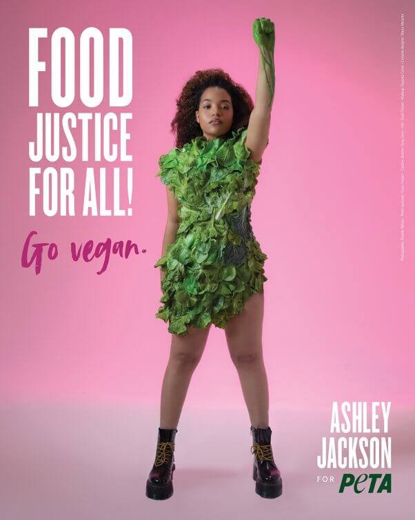 Ashley Jackson wearing lettuce dress with "food justice for all! Go Vegan" in white text on the left. Pink background