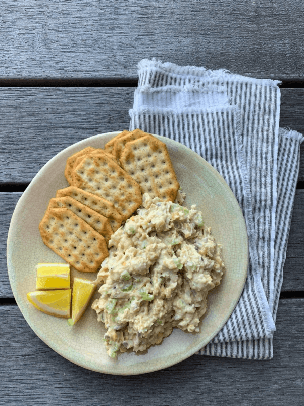 a plate with vegan chickpea tuna salad, crackers, and lemon wedges