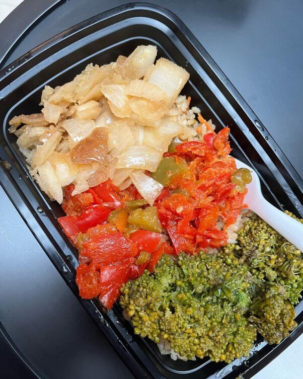 takeout container filled with sauteed vegetables on a bed of rice