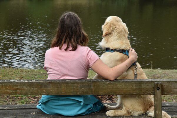 dog in blue harness and woman look out at lake together. death of a pet, pet memorial day