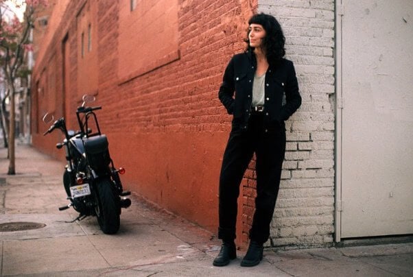 woman modeling a black vegan motorcycle jacket with a motorcycle in the background