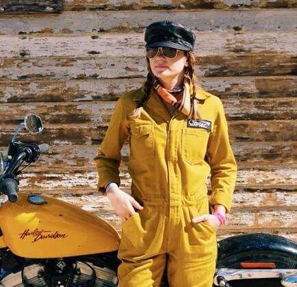 woman wearing yellow jumpsuit from stellar moto brand standing in front of a yellow motorcycle