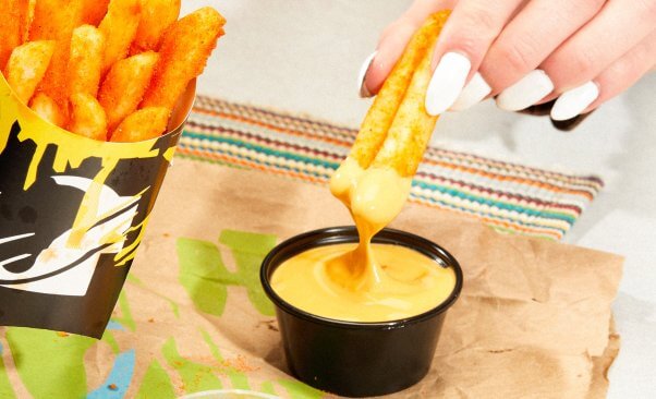 hand dipping vegan nacho fries into a dairy-free cheese sauce from taco bell
