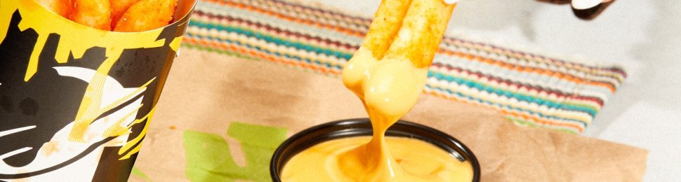 hand dipping vegan nacho fries into a dairy-free cheese sauce from taco bell