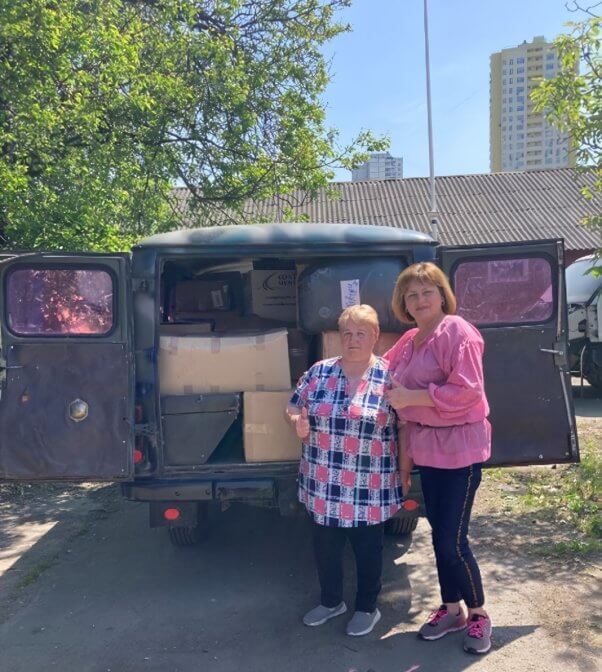 teams supported by PETA donating fur coats to Ukraine, showing two people standing behind an open van filled with boxes of coats and accessories