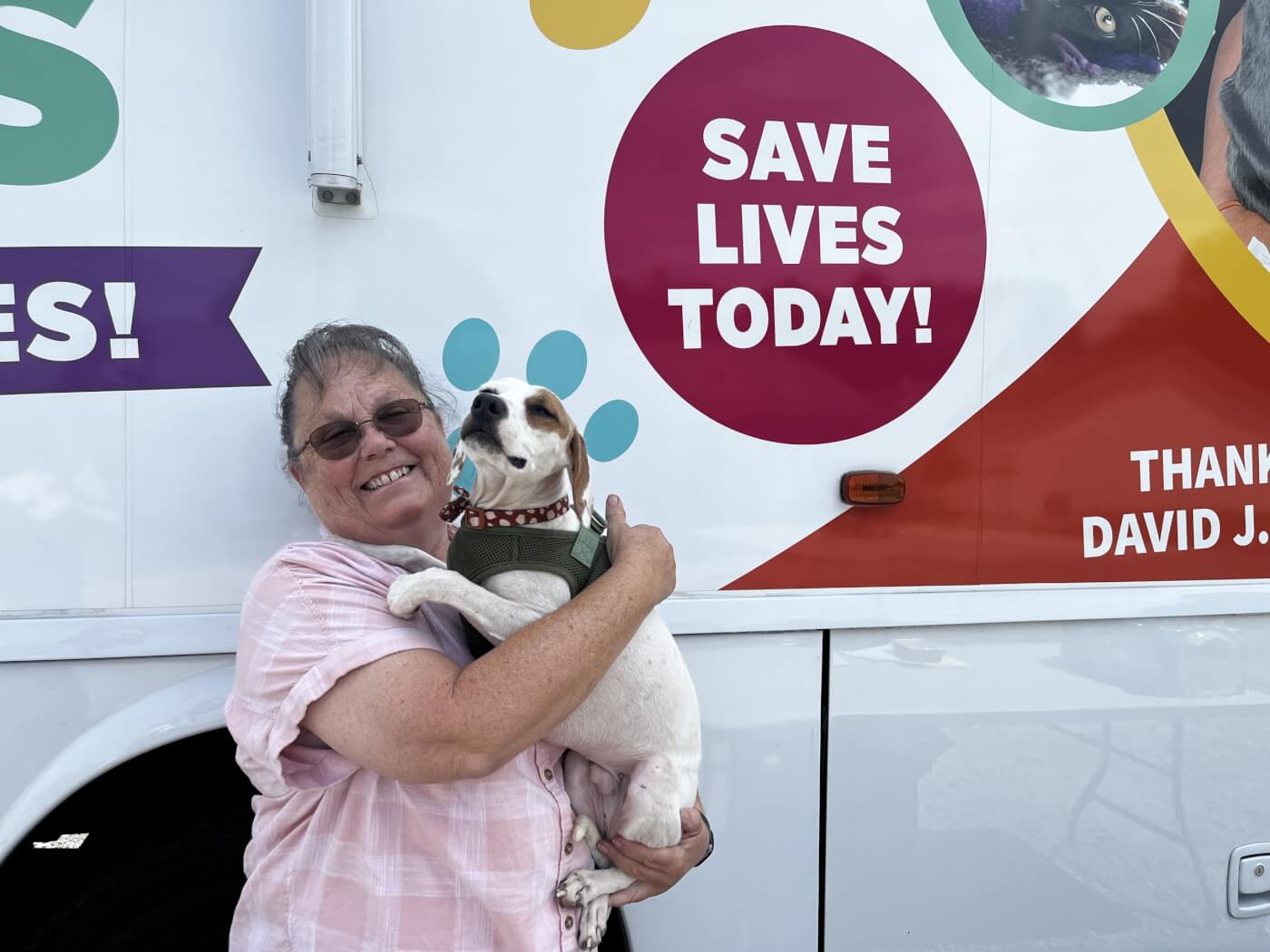 A person holds a small dog next to the PETA mobile clinic bus.