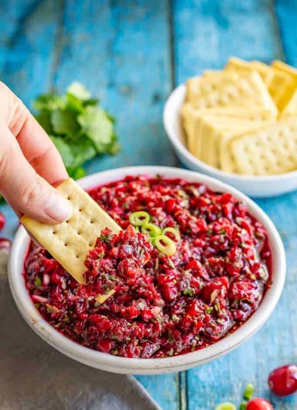 hand dipping a cracker into a bowl of fresh cranberry salsa