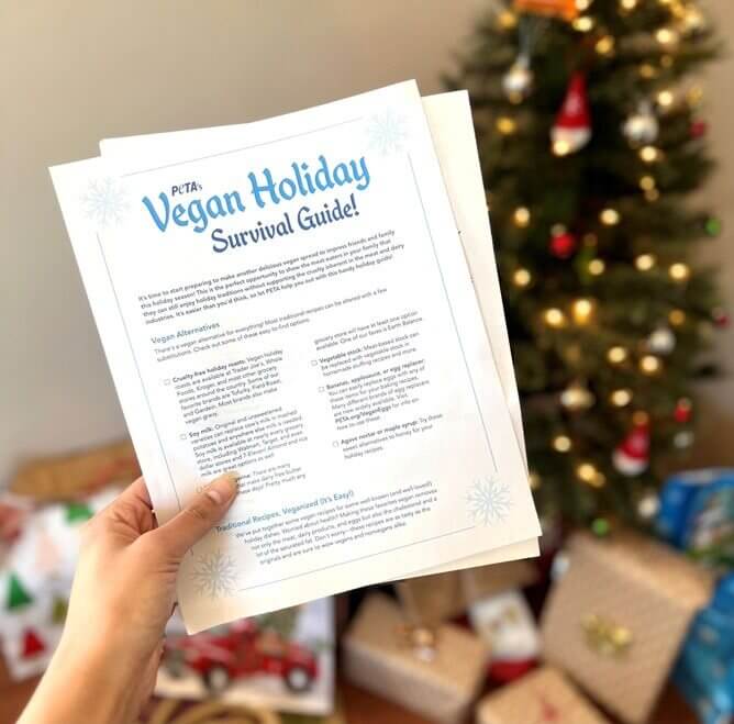 In front of a decorated tree a hand holds PETA's Vegan Holiday Survival Guide
