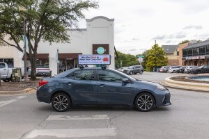 side view of a car with a banner anchored on top. The banner has a mock image of a bag with a cow's head and legs with text reading was she killed to make your carry on