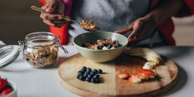 woman preparing a bowl of healthy vegan cereal, with sliced apples, bananas, and blueberries