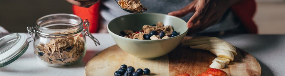 woman preparing a bowl of healthy vegan cereal, with sliced apples, bananas, and blueberries