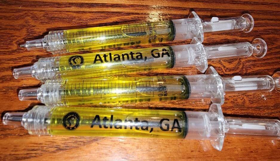 syringe shaped pens filled with a yellow liquid and the text Atlanta GA printed along the side