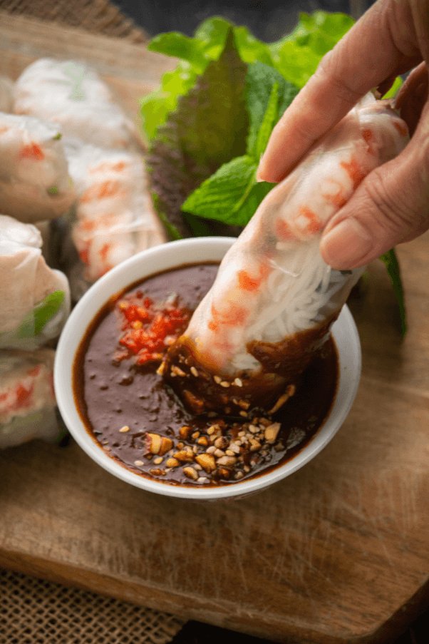 a vegan Vietnamese riced paper roll being dipped into a brown sauce