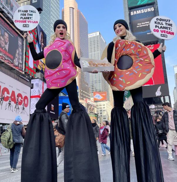 Dos seguidores de PETA vestidos como donuts y parados sobre zancos