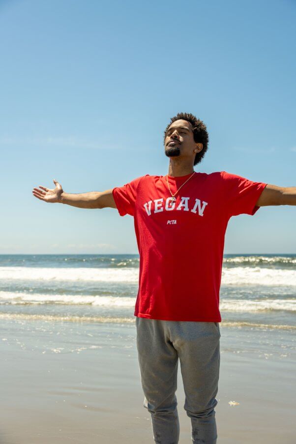 Rapper C5 standing with arms outstretched in front of the ocean
