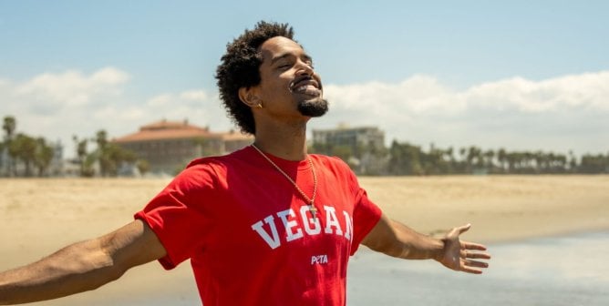 Rapper C5 standing with arms outstretched on the beach