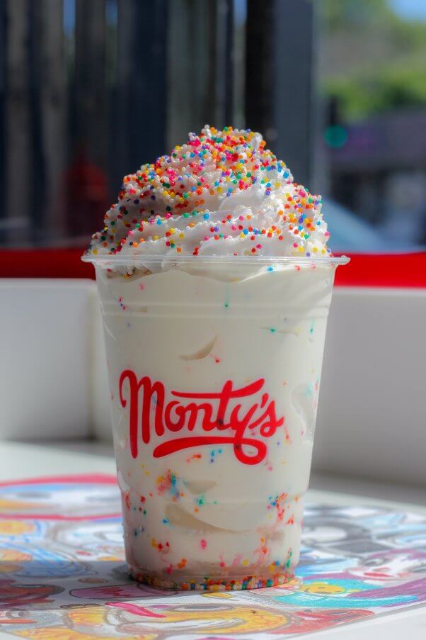 Close up of Monty's shake, a white cup with whipped cream and rainbow sprinkles