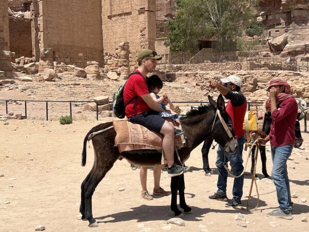 A tourist and a child sitting on a donkey's back