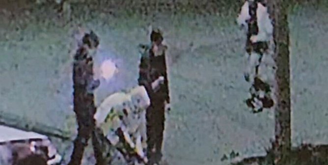 2nd-story surveillance footage still of four apparent teenagers on a nighttime neighborhood sidewalk one pointing a gun at a blurred subject