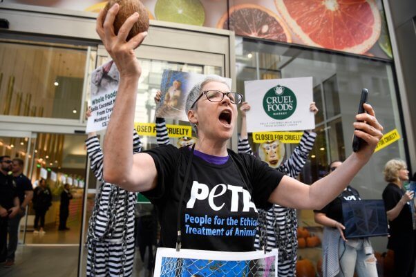 A PETA demonstrator stands in front of a Whole Foods holding a coconut
