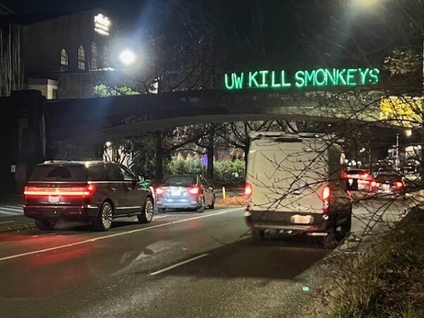 A light up sign above a freeway reading "UW Kills Monkeys"