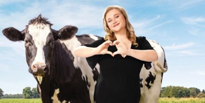 Danielle making a heart with her hands and standing next to a cow