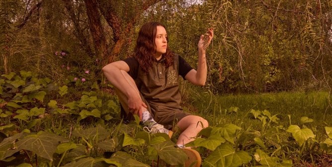 Bella Ramsey sitting in a green forestscape
