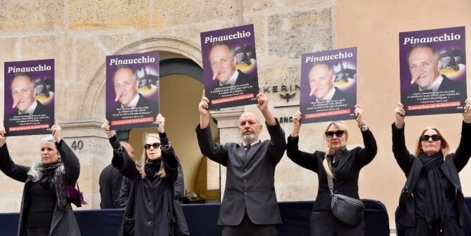 Activists hold up signs showing Kering CEO with a Pinocchio like nose