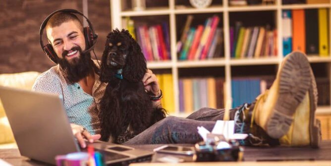 Mon in headphones with a dog in his lap working on a laptop