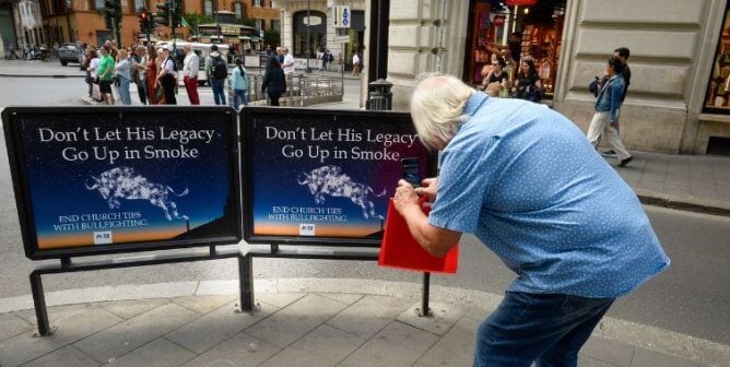 A person photographing small billboards that read "Don't Let His Legacy Go Up in Smoke"