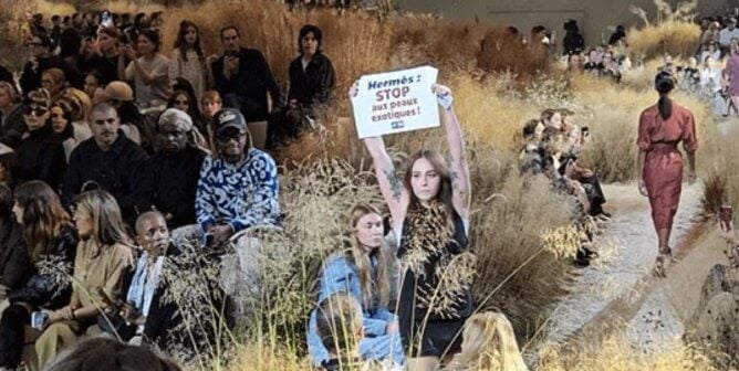Protester at Hermes runway show holds up sign