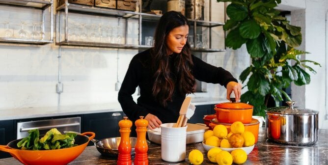 A woman cooking with an orange pots and pans set