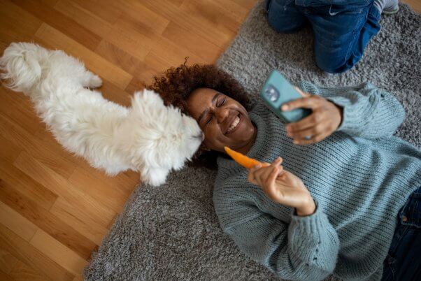 Woman on phone feeding cute white dog a carrot