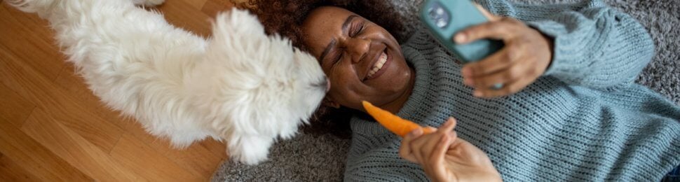 Woman on phone feeding cute white dog a carrot