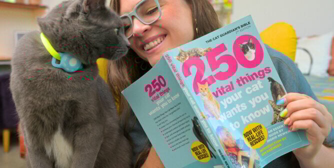 A person holding Ingrid's cat book as a cat approaches her