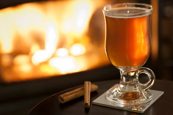 Mulled apple cider and cinnamon sticks in front of fireplace