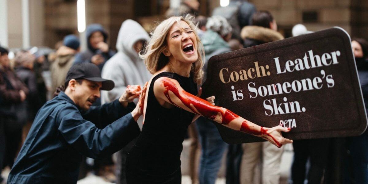 A woman being mock-skinned and while holding a sign that says "Coach: Leather is someone's skin"