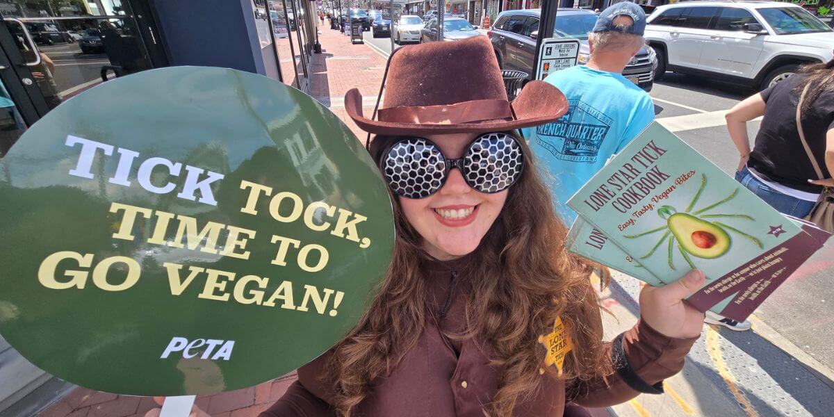 A person in a lone star tick costume holding a sign that says "Tick Tock, Time to Go Vegan"