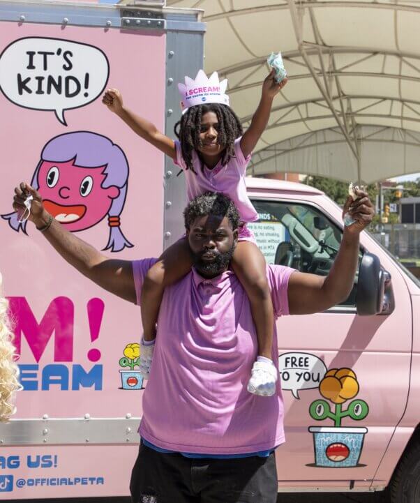 man holds child on his shoulders as they cheer
