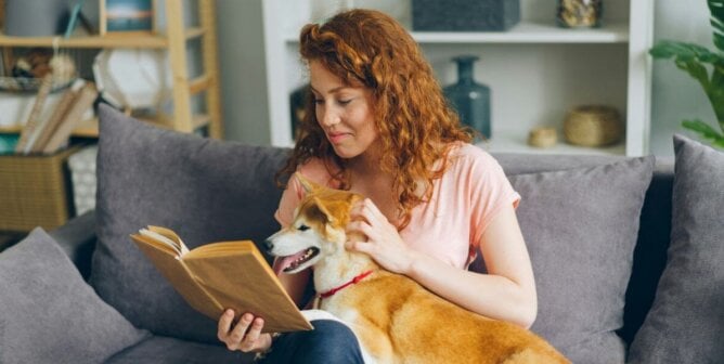 A person reading a book with a dog in their lap