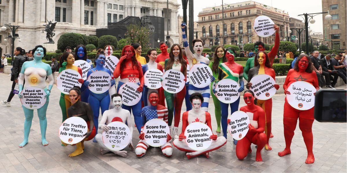 Demonstrators in country flag themed body paint holding signs that say "Score for Animals, Go Vegan!" in various languages